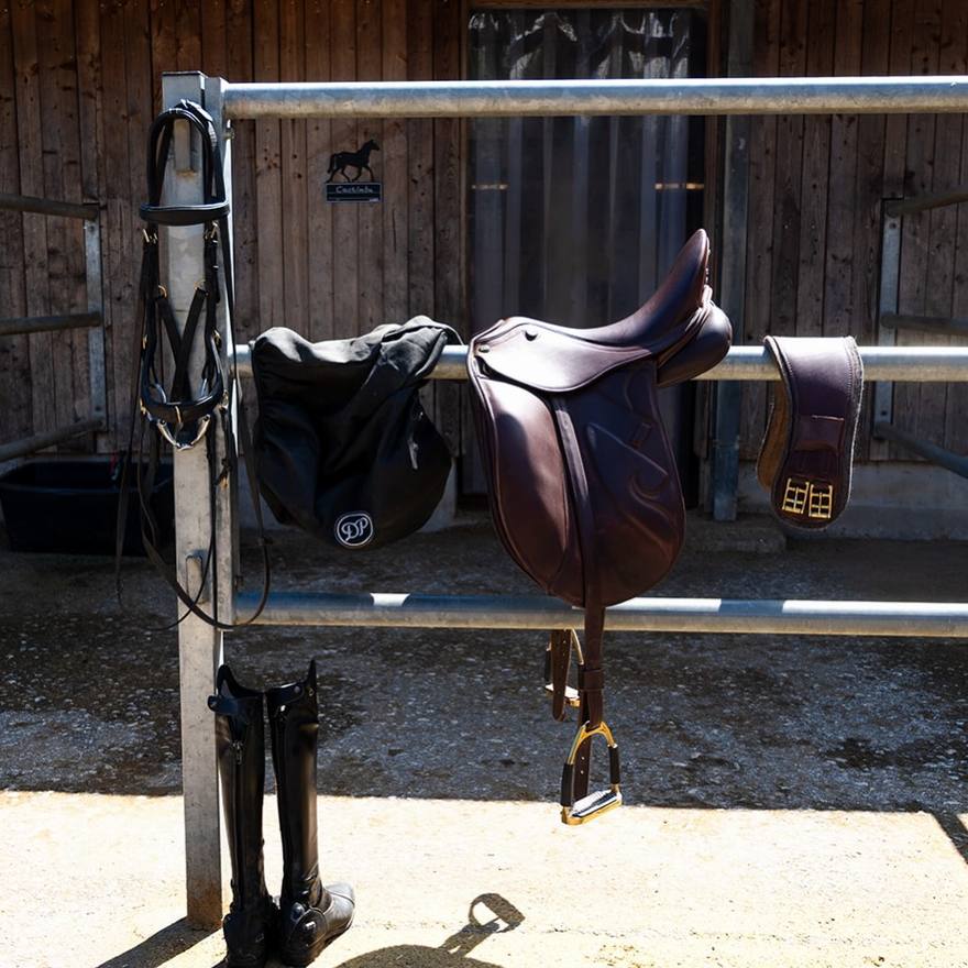 Sättel, Trensen und Reitstiefel an der Stallwand